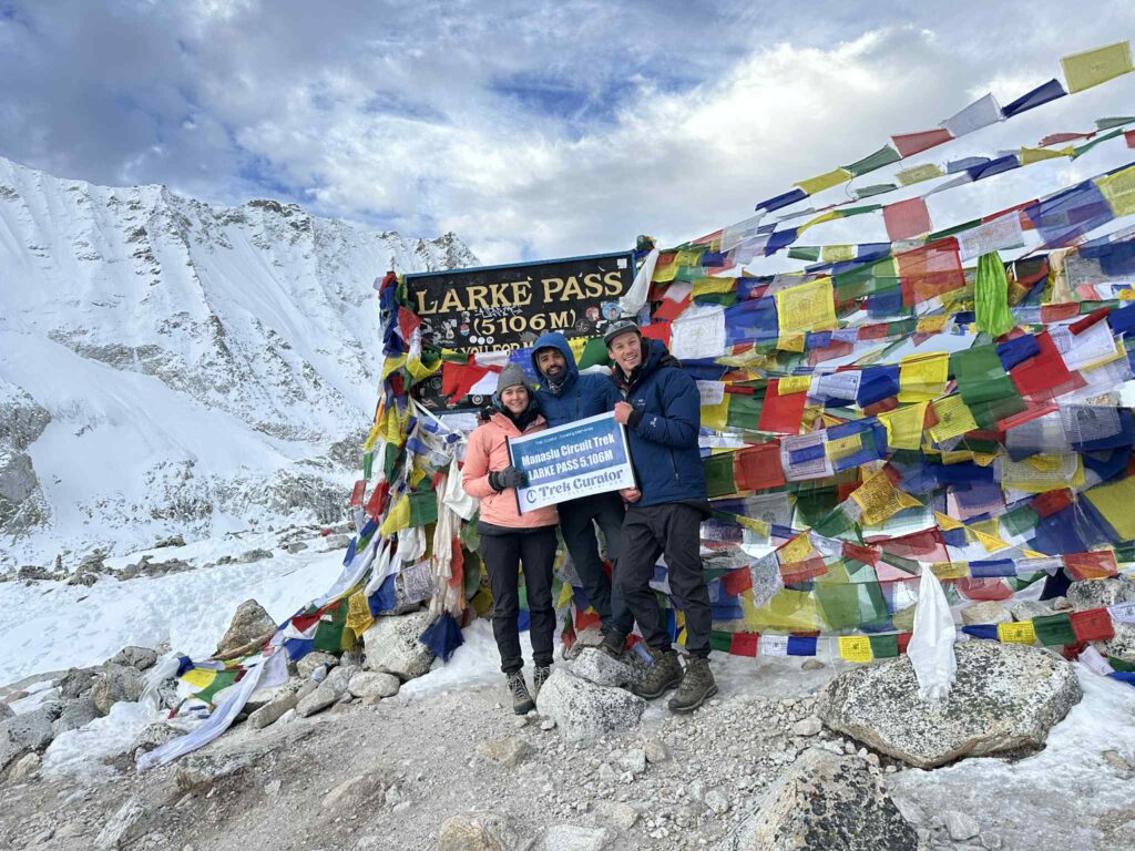 Trekkers walking across the high-altitude Larke Pass, surrounded by snowfields and steep rocky peaks along the Manaslu Circuit.